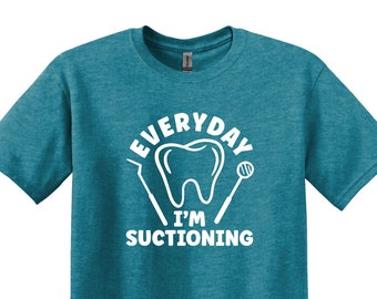 May include: A teal blue t-shirt with a white graphic of a tooth and dental tools. The text on the shirt reads "Everyday I'm Suctioning".