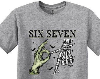 以下が含まれることがあります： 「SIX SEVEN」の文字と、OKサインをする緑色の手と骸骨の手のグラフィックがプリントされたスポーツグレーのTシャツ。デザインにはコウモリが含まれています。