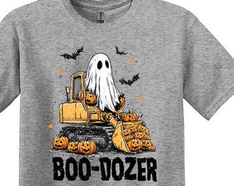 Peut inclure: T-shirt gris sport avec un motif d'Halloween. Le design présente un fantôme conduisant un engin de chantier rempli de citrouilles, avec le texte "BOO-DOZER" en dessous. Des chauves-souris et des détails orange complètent le design.