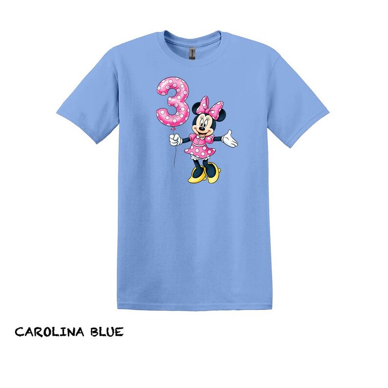 May include: Carolina blue t-shirt with a Minnie Mouse graphic holding a pink number 3 balloon. Minnie Mouse is wearing a pink polka dot dress and bow. The text "CAROLINA BLUE" is at the bottom of the image.
