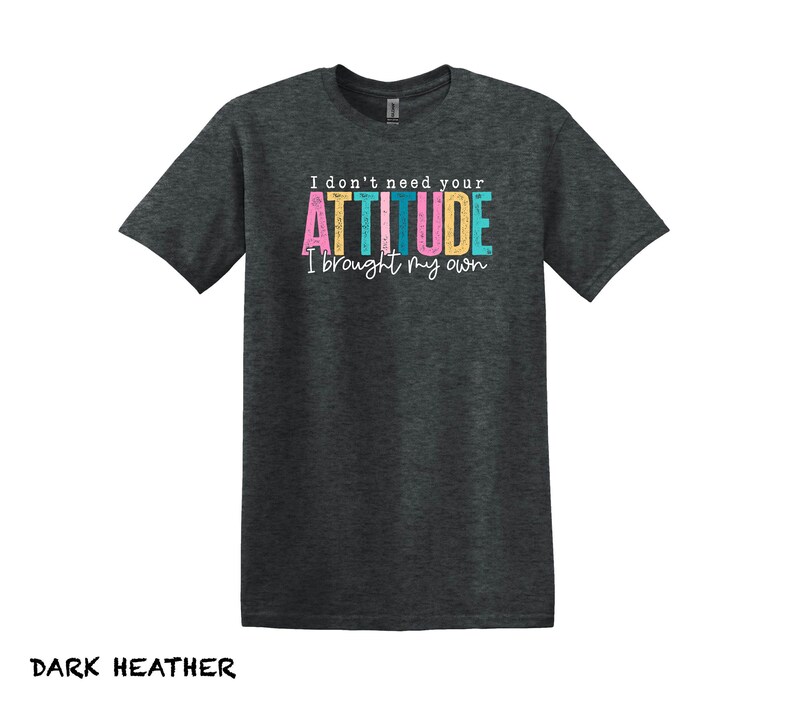 K&ouml;nnte beinhalten: Dunkelgraues T-Shirt mit dem Text "I don't need your ATTITUDE I brought my own" in bunten Buchstaben.