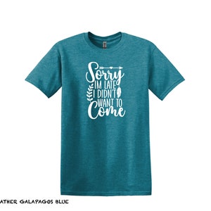 K&ouml;nnte beinhalten: Ein blaues T-Shirt mit dem Text "Sorry, ich bin zu sp&auml;t, ich wollte nicht kommen" in wei&szlig;en Buchstaben mit einem kleinen Pfeil- und Federdesign.