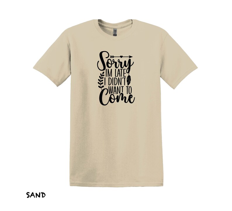K&ouml;nnte beinhalten: Ein sandfarbenes T-Shirt mit einer schwarzen Grafik, auf der "Sorry, ich bin zu sp&auml;t, ich wollte nicht kommen" steht, mit einem kleinen Pfeil und einem Federdesign.