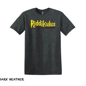 Pode incluir: Camiseta cinza escuro com o texto "Riddikulus" em letras amarelas e uma varinha marrom por baixo.