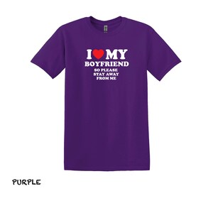 May include: Purple t-shirt with white text that reads "I love my boyfriend so please stay away from me". A red heart is in the text.