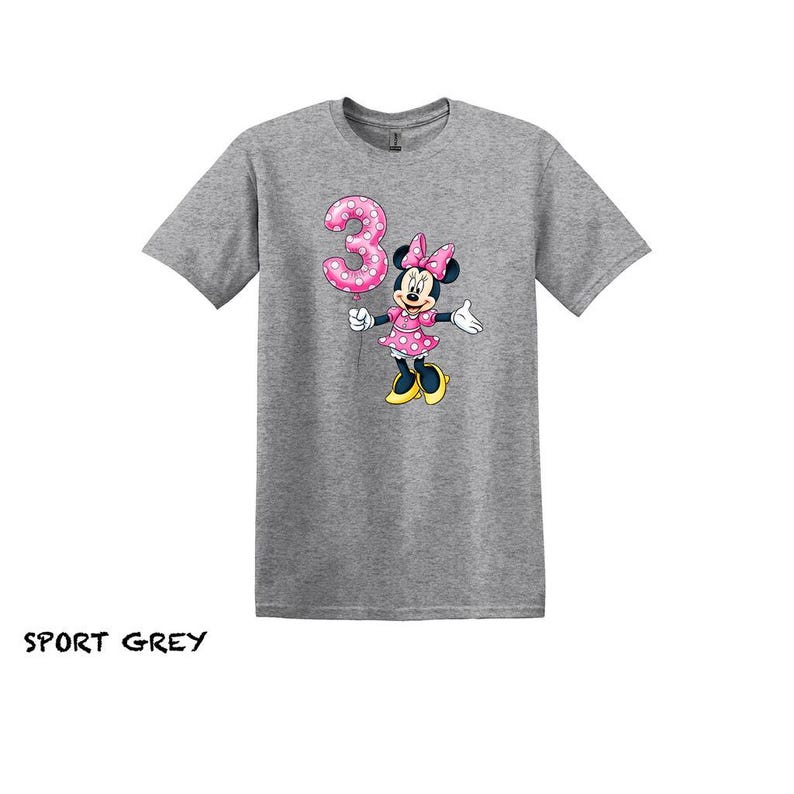 May include: Sport grey t-shirt with a Minnie Mouse graphic holding a pink polka dot number 3 balloon. Minnie Mouse is wearing a pink polka dot dress and bow. The text "SPORT GREY" is at the bottom of the image.