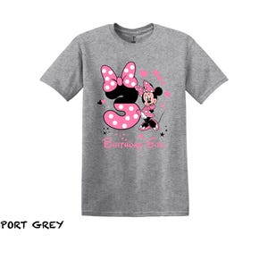 May include: A gray t-shirt with a pink and black Minnie Mouse graphic. The graphic shows Minnie Mouse holding a pink number 3 with white polka dots. The text "Birthday Girl" is below the graphic.