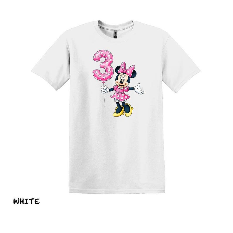 May include: White t-shirt with a cartoon Minnie Mouse holding a pink number 3 balloon. Minnie Mouse is dressed in a pink polka dot dress and bow. The word "WHITE" is printed at the bottom of the shirt.