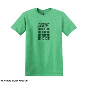 K&ouml;nnte beinhalten: Ein gr&uuml;nes T-Shirt aus Heather-Material mit dem Text "IF YOU CAN READ THIS, YOU ARE TOO..." und einer Reihe von Bin&auml;rcode: "01000111 01100101 01100101 01101011".