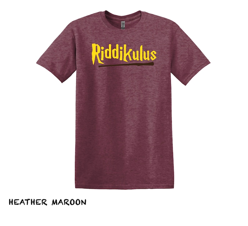 Pode incluir: Uma camiseta de cor marrom heather com o texto "Riddikulus" em letras amarelas e um gr&aacute;fico de varinha marrom.