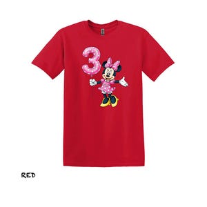 May include: Red t-shirt with a Minnie Mouse graphic holding a pink number 3 balloon. Minnie Mouse is wearing a pink polka dot dress and bow. The word "RED" is printed at the bottom of the shirt.