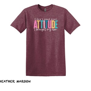 K&ouml;nnte beinhalten: T-Shirt in Heidelbeer-Maroon mit dem Text "I don't need your ATTITUDE I brought my own" in bunten Buchstaben.