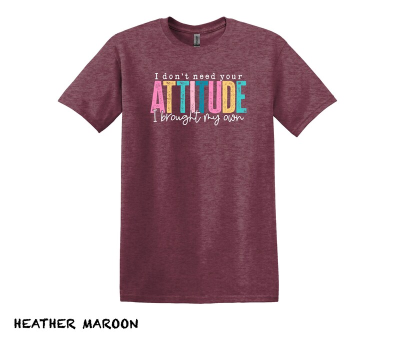 K&ouml;nnte beinhalten: T-Shirt in Heidelbeer-Maroon mit dem Text "I don't need your ATTITUDE I brought my own" in bunten Buchstaben.