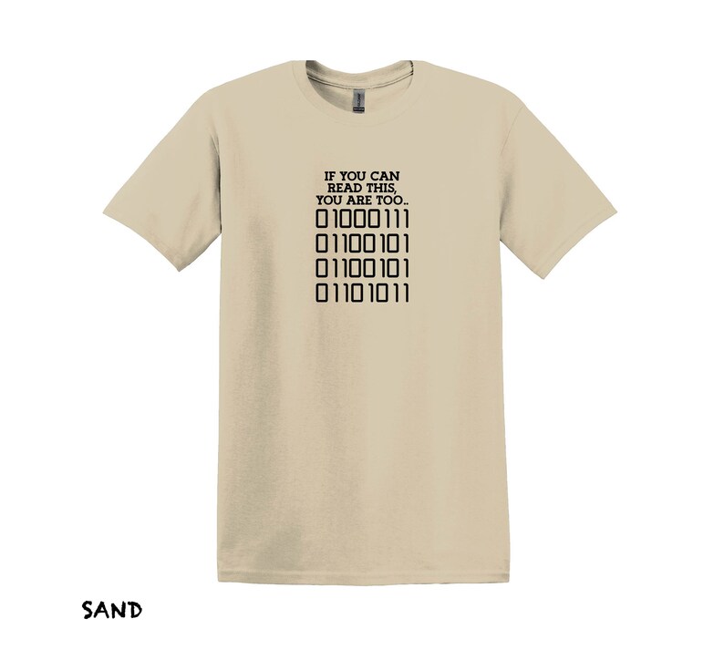 K&ouml;nnte beinhalten: Ein beiges T-Shirt mit einem schwarzen Aufdruck, der "IF YOU CAN READ THIS, YOU ARE TOO..." lautet, und einer Reihe von Bin&auml;rcode: "01000111 01100101 01100101 01101011".