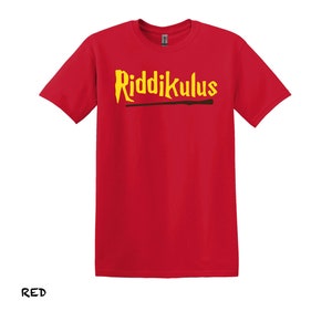 Pode incluir: Camiseta vermelha com o texto "Riddikulus" em letras amarelas e um gr&aacute;fico de varinha marrom.
