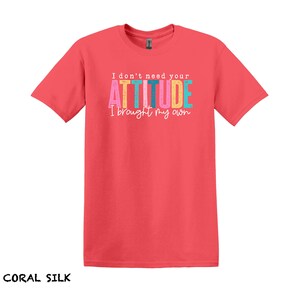 K&ouml;nnte beinhalten: Coralfarbenes Seiden-T-Shirt mit dem Text "I don't need your ATTITUDE I brought my own" in bunten Buchstaben.