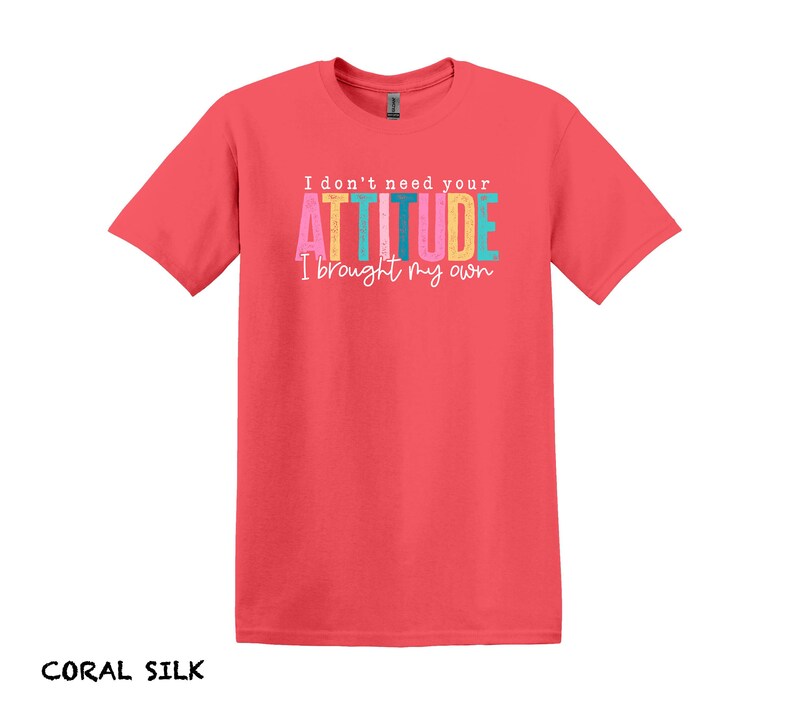 K&ouml;nnte beinhalten: Coralfarbenes Seiden-T-Shirt mit dem Text "I don't need your ATTITUDE I brought my own" in bunten Buchstaben.