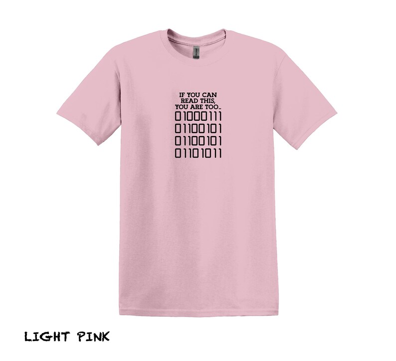 K&ouml;nnte beinhalten: Ein hellrosa T-Shirt mit dem Text "IF YOU CAN READ THIS, YOU ARE TOO..." und einer Reihe von Bin&auml;rcode: "01000111 01100101 01100101 01101011".