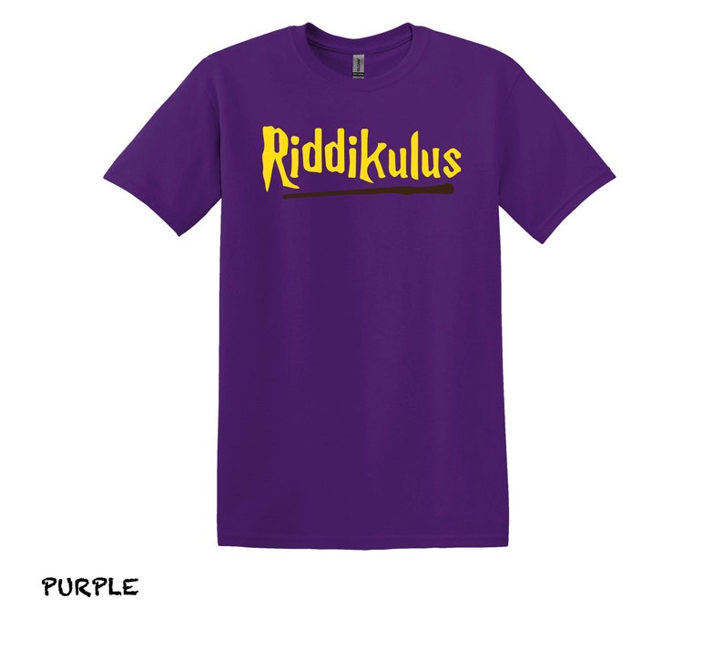 Pode incluir: Camiseta roxa com o texto "Riddikulus" em letras amarelas e um gr&aacute;fico de varinha marrom.