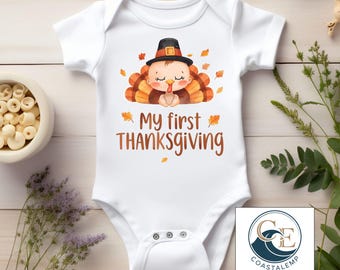 May include: White baby bodysuit with a Thanksgiving turkey graphic. The design features a cartoon turkey wearing a pilgrim hat, with the text "My first THANKSGIVING". The bodysuit has short sleeves and snap closures.