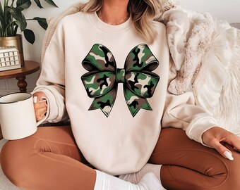May include: A cream-colored sweatshirt with a large green and brown camouflage bow design.