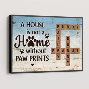 May include: A framed wooden sign with a blue and white background. The sign reads "A HOUSE is not a HOME without PAW PRINTS." Scrabble tiles spell out "BUDDY", "BAILEY", "PEANUT", and "Y". A paw print and heart are also featured.