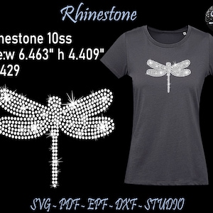 Puede incluir: Diseño de libélula de pedrería para una camiseta. El diseño tiene 16,41 cm de ancho y 11,20 cm de alto. El diseño está compuesto por 429 pedrerías.