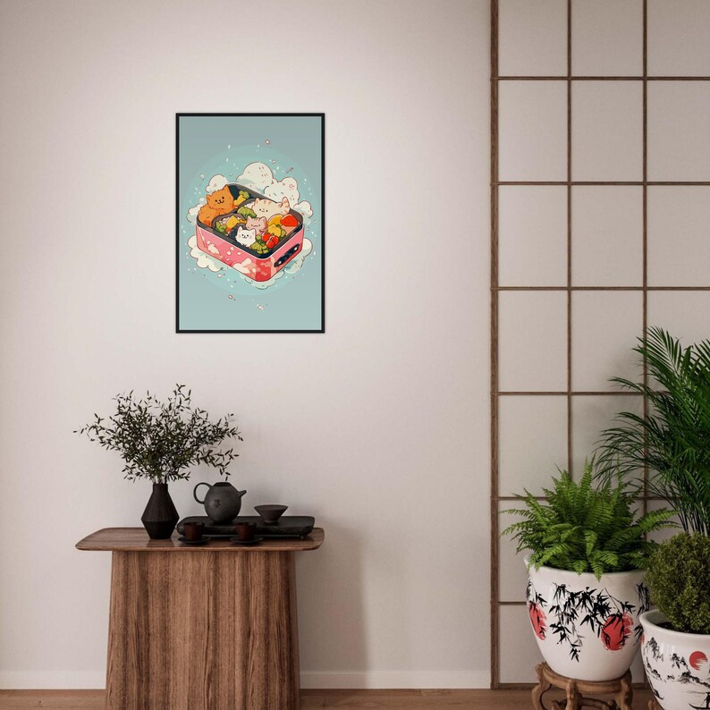 May include: A framed illustration of a pink bento box filled with cartoon cats and food. The cats are in various poses and the food includes vegetables, rice, and fish. The background is a light blue with white clouds and pink cherry blossoms.