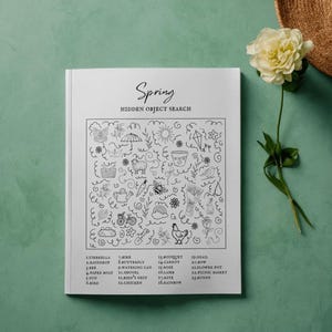 May include: A white book titled "Spring Hidden Object Search" with a detailed black and white illustration. The image includes a straw hat and a white and yellow flower on a green background. The book features a list of objects to find.