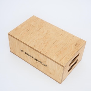 Può includere: Una scatola di legno con la scritta "STUDIO FREIBURGER" stampata sul lato. La scatola ha due maniglie tagliate sul lato.