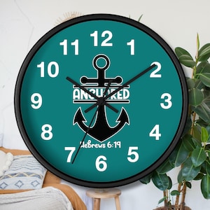 Op de afbeelding: Een ronde turquoise wandklok met zwarte cijfers en wijzers. De klok heeft een zwart anker met het woord "Anchored" en de tekst "Hebrews 6:19" onder het anker.