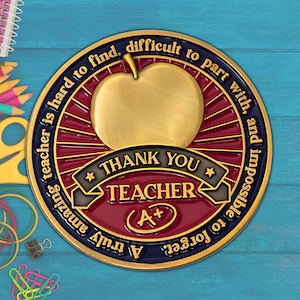 May include: A gold-colored apple-shaped teacher appreciation medallion with the words "Thank You Teacher" and "A+". The medallion has a red and navy blue border with text that reads "A truly amazing teacher is hard to find, difficult to part with, and impossible to forget."