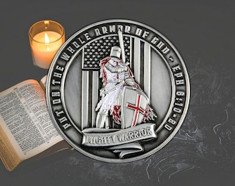 Puede incluir: Una moneda plateada con un caballero con armadura sosteniendo una espada y un escudo con una cruz roja. La moneda tiene el texto "PUT ON THE WHOLE ARMOR OF GOD" y "MIGHTY WARRIOR". Una vela encendida y un libro abierto en el fondo.