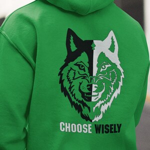 以下が含まれることがあります： 背面に黒と白のオオカミのグラフィックが描かれた緑色のフード付きスウェットシャツ。オオカミの顔は半分に分割され、片側は黒、もう片側は白です。オオカミの下には「CHOOSE WISELY」というテキストが印刷されています。