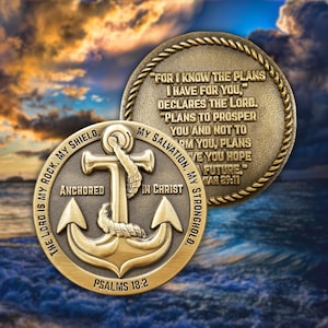 May include: Two bronze-colored coins with religious inscriptions. One coin features an anchor design with the words "Anchored in Christ" and "Psalms 18:2." The other coin has a quote from Jeremiah 29:11. The background shows a seascape with a cloudy sky.