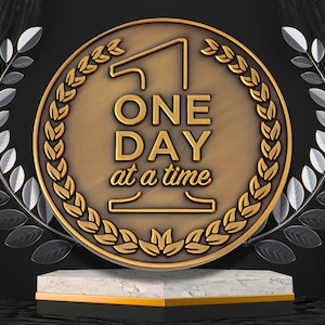 Puede incluir: Medallón dorado con la frase "ONE DAY at a time". Rodeado por una corona de laurel y hojas plateadas. Se exhibe sobre un pedestal de mármol y oro, con un fondo negro.