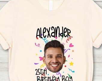 May include: Cream-colored t-shirt with the text "Alexander" above a smiling man's face, with "25th Birthday Boy" below. Colorful confetti and stars surround the face. The shirt has a crew neck and short sleeves.