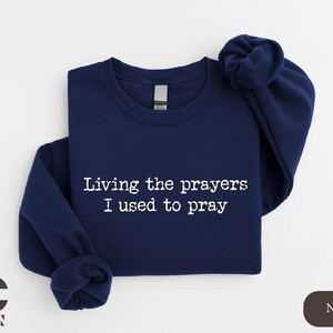 a navy sweatshirt with white writing that says living the prayer i used to pray