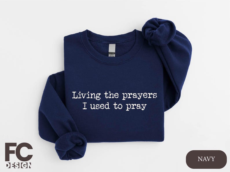 a navy sweatshirt with white writing that says living the prayer i used to pray