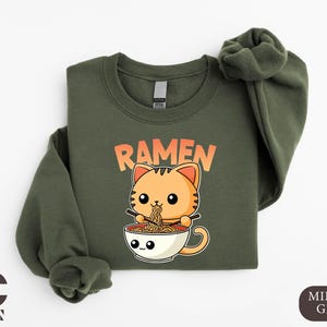 a green shirt with a cat in a cup of ramen