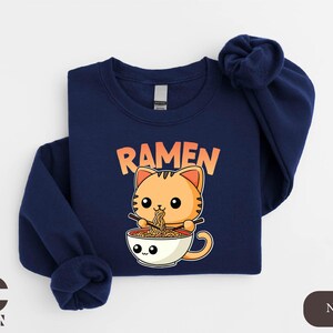 a blue shirt with a cat eating ramen out of a bowl