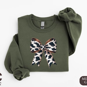 May include: A green sweatshirt with a brown and white leopard print bow on the front.