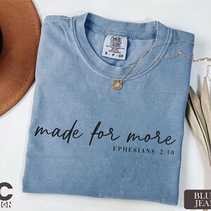 a blue t-shirt with the text "made for more" printed on it, along with a necklace and a hat.