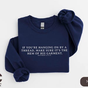 May include: Navy blue sweatshirt with the text "If you're hanging on by a thread, make sure it's the hem of his garment. Matthew 9:20-22" printed in white.