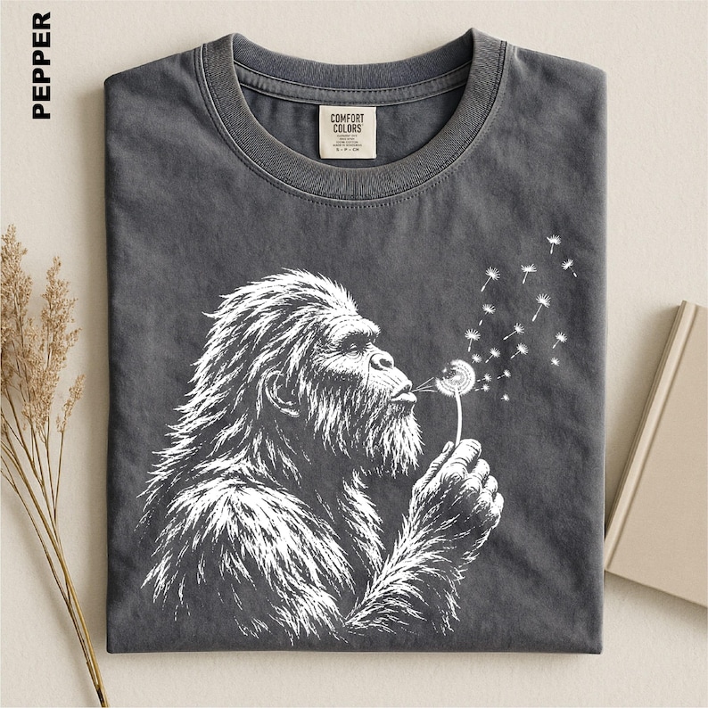 a gray t-shirt with a white illustration of a gorilla blowing a dandelion on it.