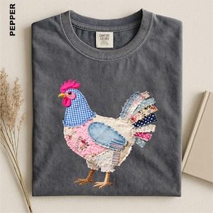 May include: A charcoal gray crew neck t-shirt featuring a patchwork-style chicken graphic. The chicken is composed of various fabric patterns including blue gingham, pink floral, denim, and striped textures. The shirt has a Comfort Colors brand label.