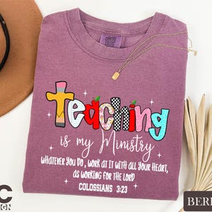May include: Berry-colored t-shirt with the words "Teaching is my Ministry" in a colorful, playful font. The shirt also features the text "Whatever you do, work at it with all your heart, as working for the Lord, Colossians 3:23."