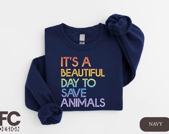 Könnte beinhalten: Navyblauer Sweatshirt mit dem Text "It's a beautiful day to save animals" in Regenbogenfarben.