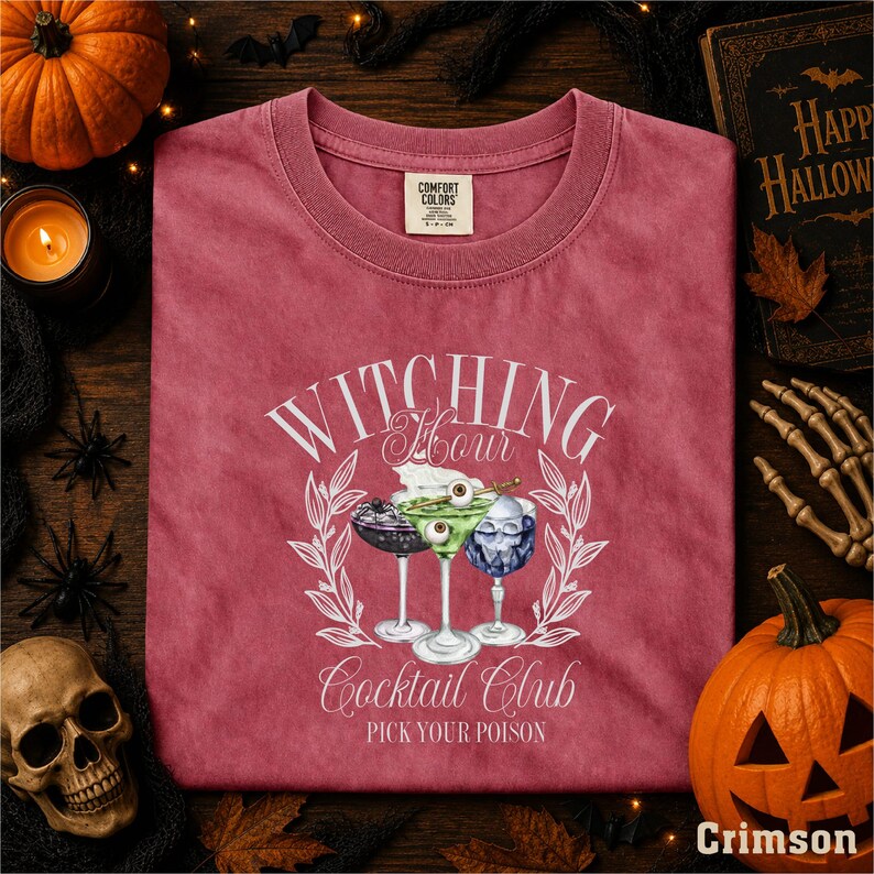 a pink t-shirt with a graphic design of a cocktail glass and the text "WITCHING YOUR COCKTAIL CLUB PICK YOUR POISON" printed on it, surrounded by Halloween-themed items such as a pumpkin, bats, and a skeleton.