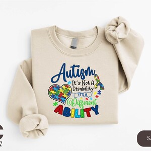 May include: A beige sweatshirt with a blue and rainbow design that says "Autism It's Not A Disability It's A Different Ability".